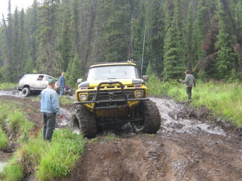 1995 Ford Bronco - Two off-road vehicles navigate a muddy trail in a forest setting.