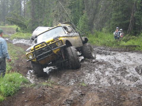 1995 Ford Bronco - A yellow 1970s Ford F-Series truck navigates a muddy off-road course with another vehicle behind it.