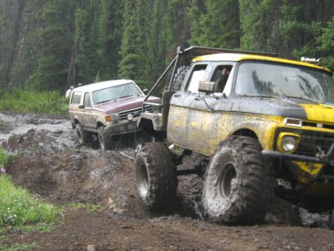 1995 Ford Bronco - Two off-road vehicles struggle through thick mud on a wooded trail.