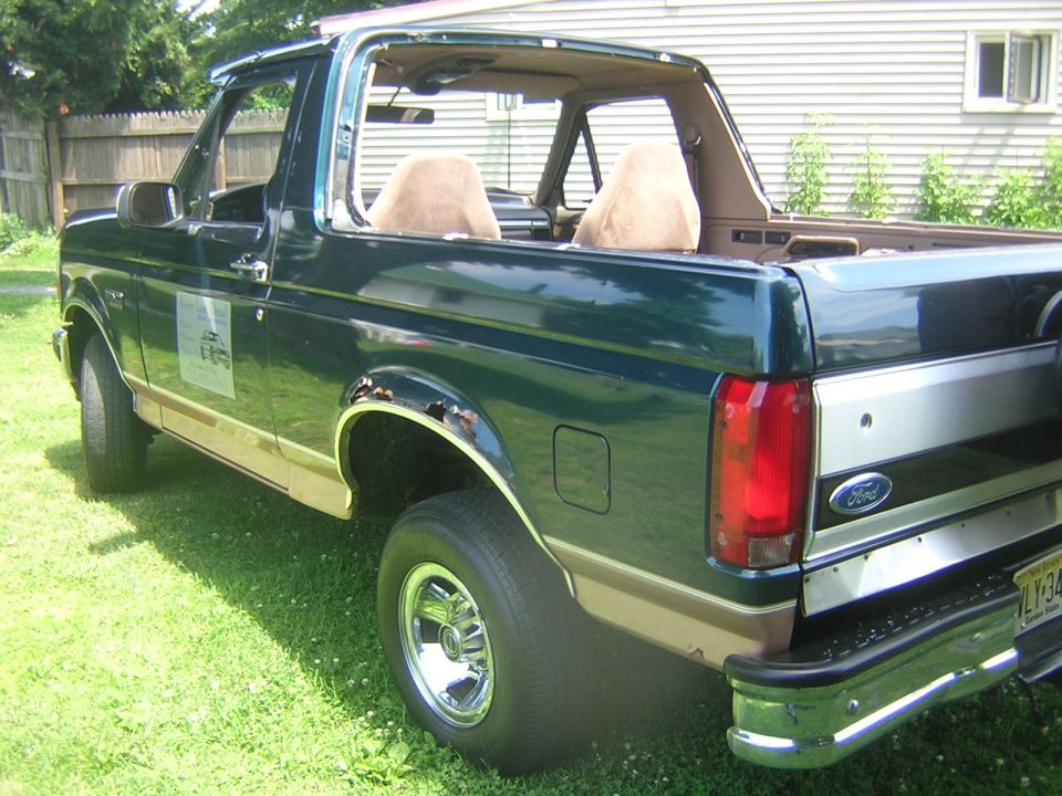 Dark green topless Ford Bronco rear quarter view with rust on wheel arch, parked on grass