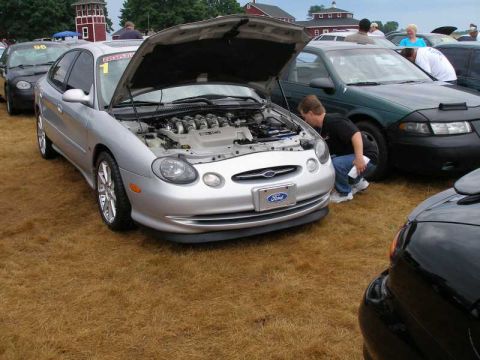 1997 Ford Taurus - Three-quarter front view of a silver Ford Taurus SHO at a grass-field car show with the hood raised, exposing the polished V8 intake manifo…