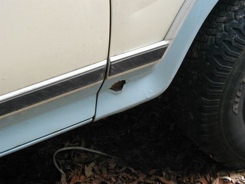 1986 Ford Bronco - Detail of a vehicle's lower door panel showing rust damage near the wheel well.