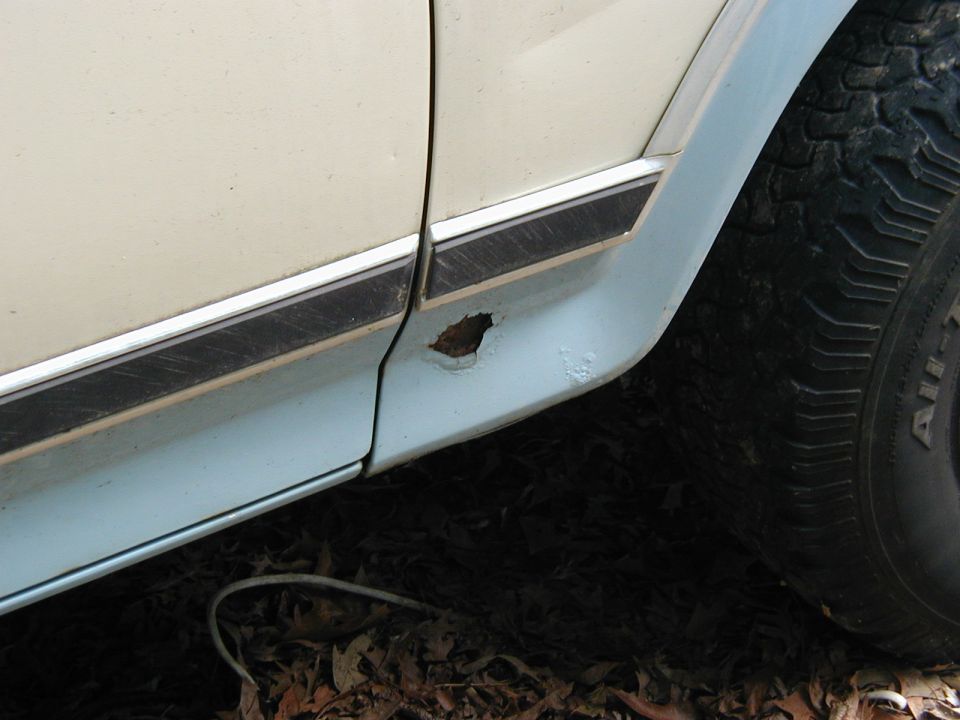 Close-up of a rusty lower door panel and tire on a light-colored vehicle