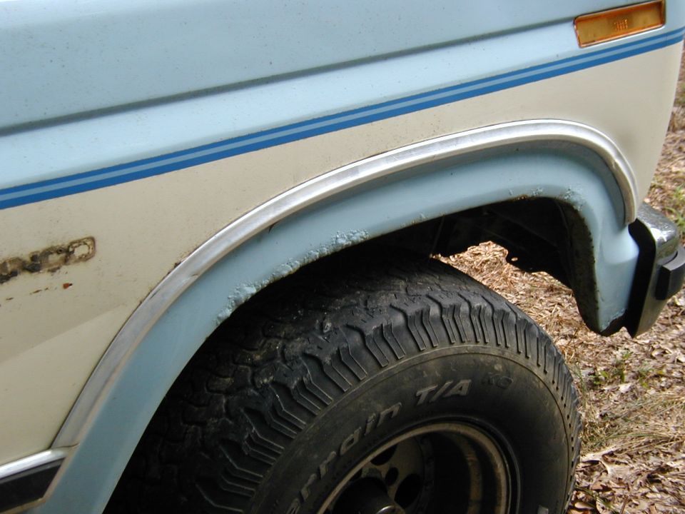 1986 Ford Bronco side view, showing fender and tire with blue and cream paint