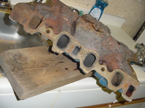 1979 Ford F-150 - A heavily rusted engine intake manifold is shown resting on a wooden block in what appears to be a kitchen or utility area.