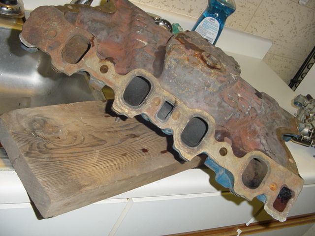 rusted engine intake manifold sitting on a wooden block next to a sink