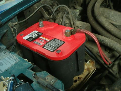 1996 Ford Bronco - A close-up view of a car battery installed in an engine compartment.