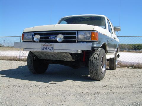 1991 Ford Bronco - Front view of a two-tone Ford Bronco with an aftermarket bumper and auxiliary lights under a clear blue sky.