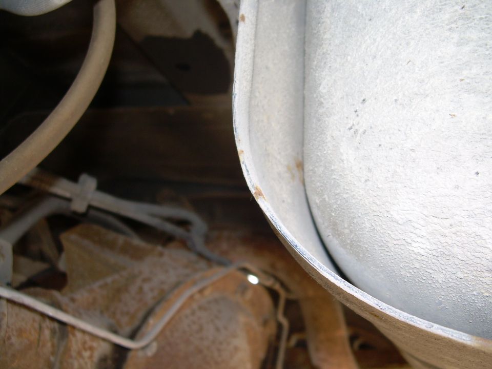 Underside of a vehicle showing exhaust pipe and rusty frame components