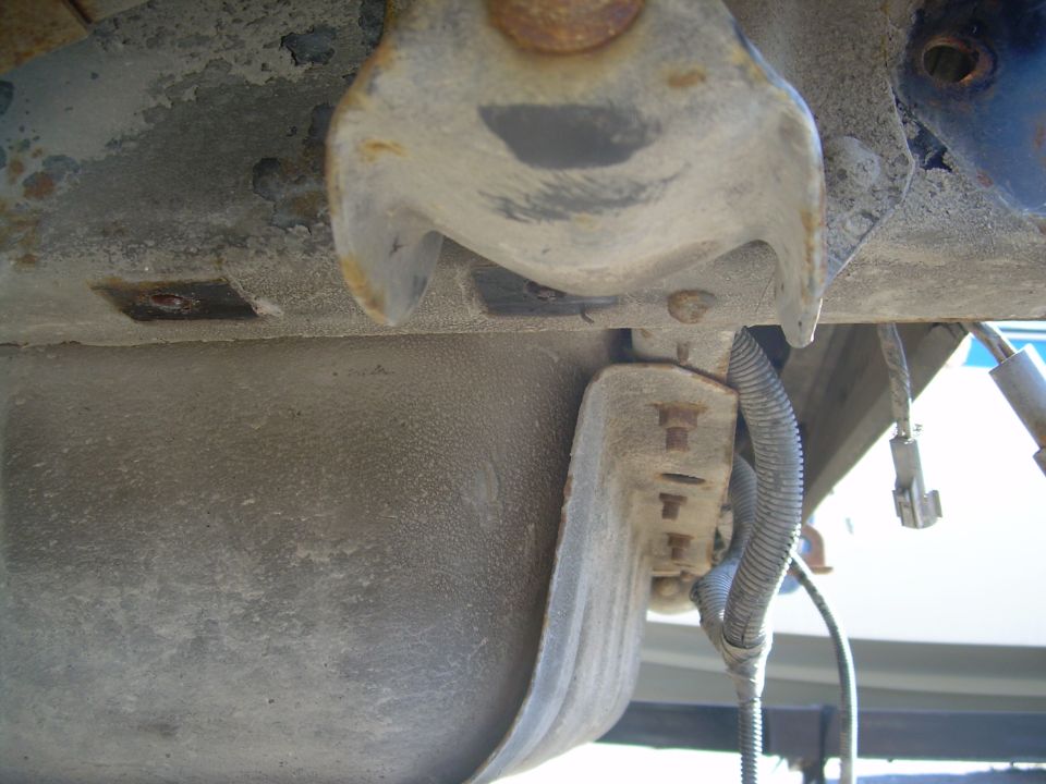 Undercarriage of a vehicle showing a fuel tank and suspension components. Some rust is visible