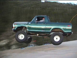 1979 Ford Bronco - Green Ford Bronco airborne over a dirt hill during an off-road event.