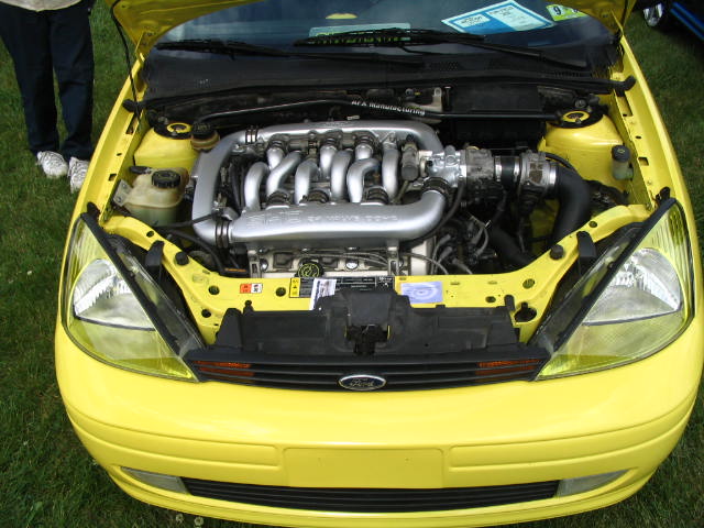Yellow Ford Focus with hood open showing polished intake manifold on a four-cylinder