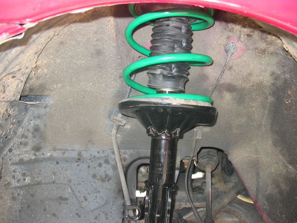 Close-up of a car's front suspension strut with a green coil spring