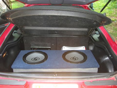 1995 Ford Probe - The interior of a red car's trunk shows a custom subwoofer setup with two speakers.