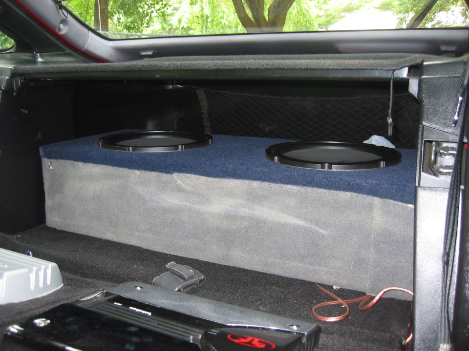 Car trunk area showing a custom subwoofer box with two speakers, amplifier, and wiring