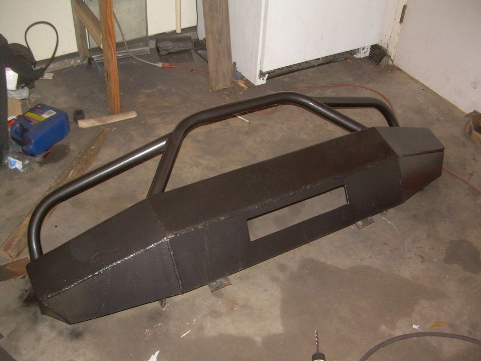 Fabricated black plate-steel front winch bumper with tube hoop and fairlead opening on a garage floor