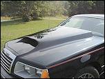 1987 Ford Thunderbird - A car with a prominent hood scoop is shown outdoors with trees and grass visible.