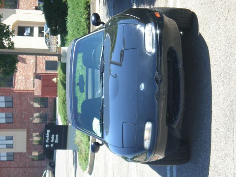 1996 Mazda Miata - A black Mazda Miata is parked outside a building. The car has pop-up headlights and a visible interior.