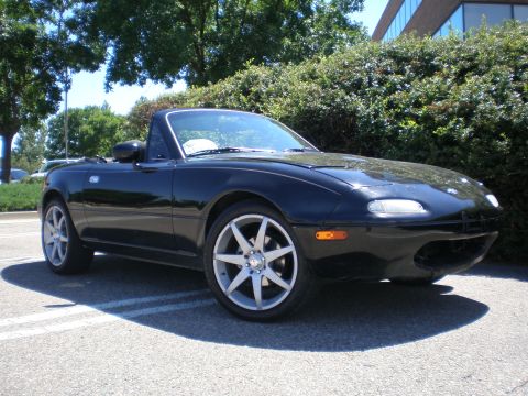 1996 Mazda Miata - A black 1996 Mazda Miata convertible is parked outdoors, showing its distinctive front end and sporty design.