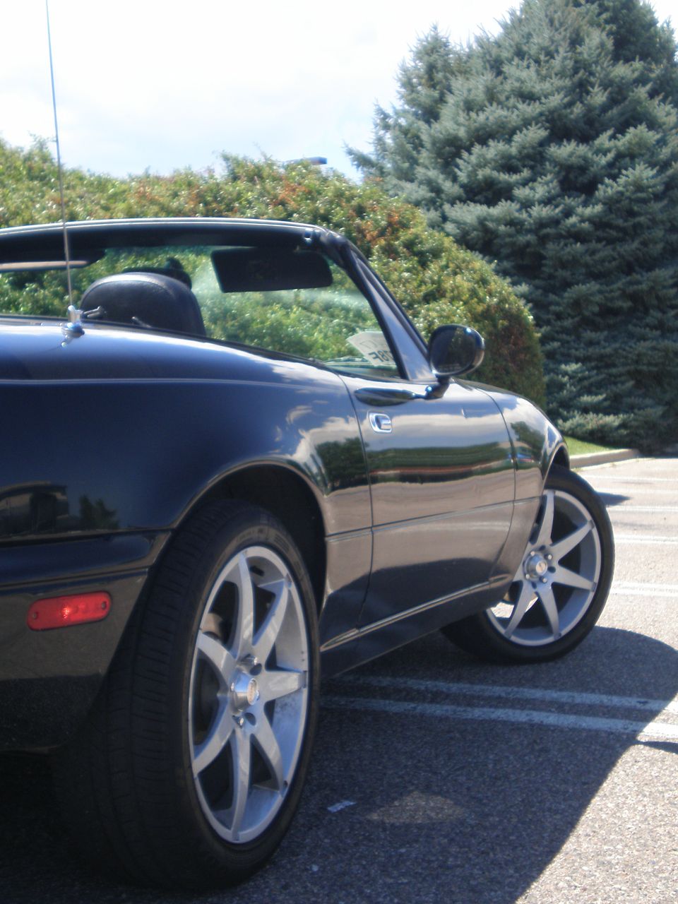 Dark convertible sports car parked outside with trees in the background