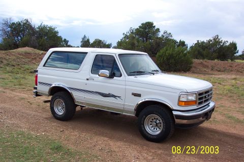 1996 Ford Bronco - This white 1996 Ford Bronco is parked on a dirt road with trees and hills in the background.