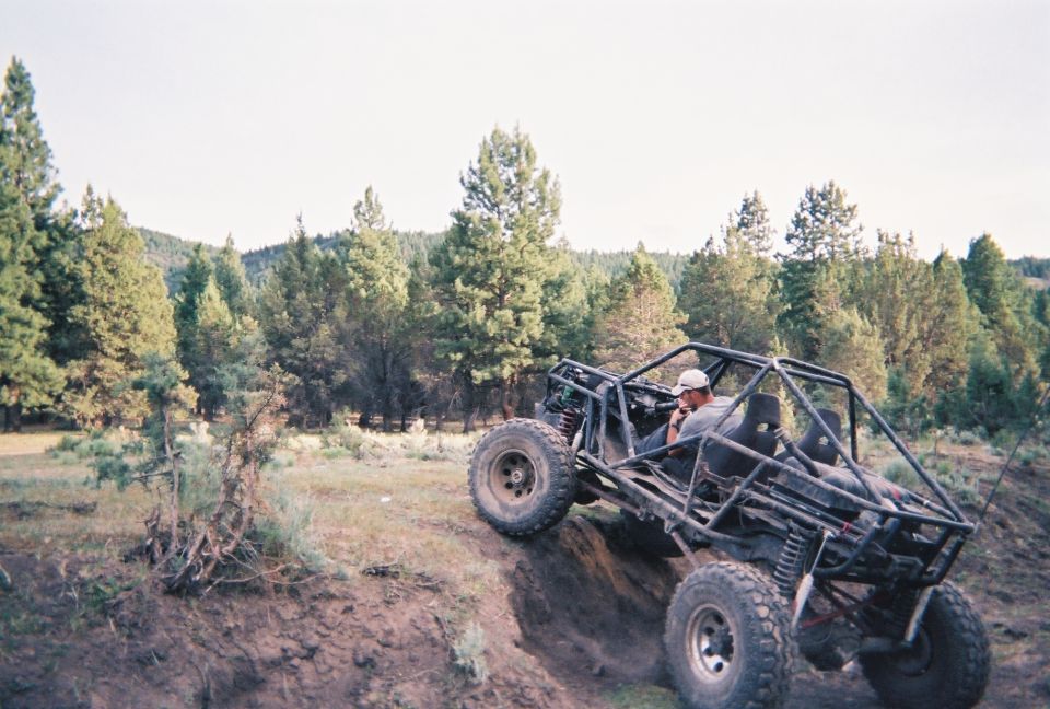 Black off-road buggy with a roll cage and large tires climbing a dirt incline, driver wearing a white cap