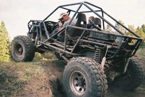 1984 Ford Bronco - A bodyless tube-chassis rock buggy with a full roll cage, coil-over shocks and mud-caked oversized off-road tires climbs a dirt bank with t…