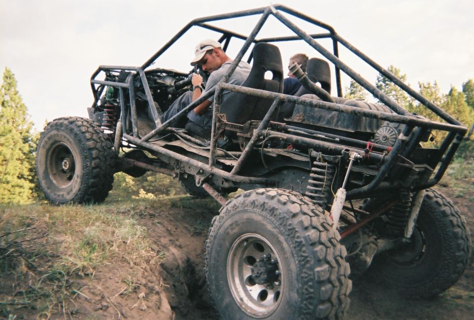 Tube-chassis rock buggy with roll cage flexing on a dirt bank off-road