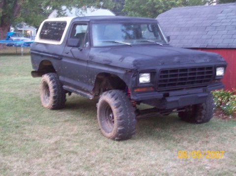Lifted 1978 Ford Bronco with aftermarket bumper and large tires parked on grass