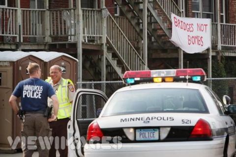 1998 Ford Crown Victoria - Two officers converse near a police vehicle, with a protest banner visible in the background.