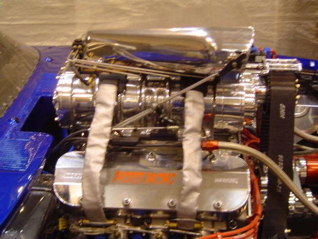 Close-up of a V8 engine with a chrome supercharger and orange 'PRO-MAX' lettering on the valve cover