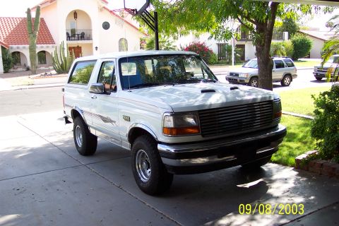 1996 Ford Bronco - A white Ford Bronco is parked in a driveway in front of a house, with other vehicles in the background.