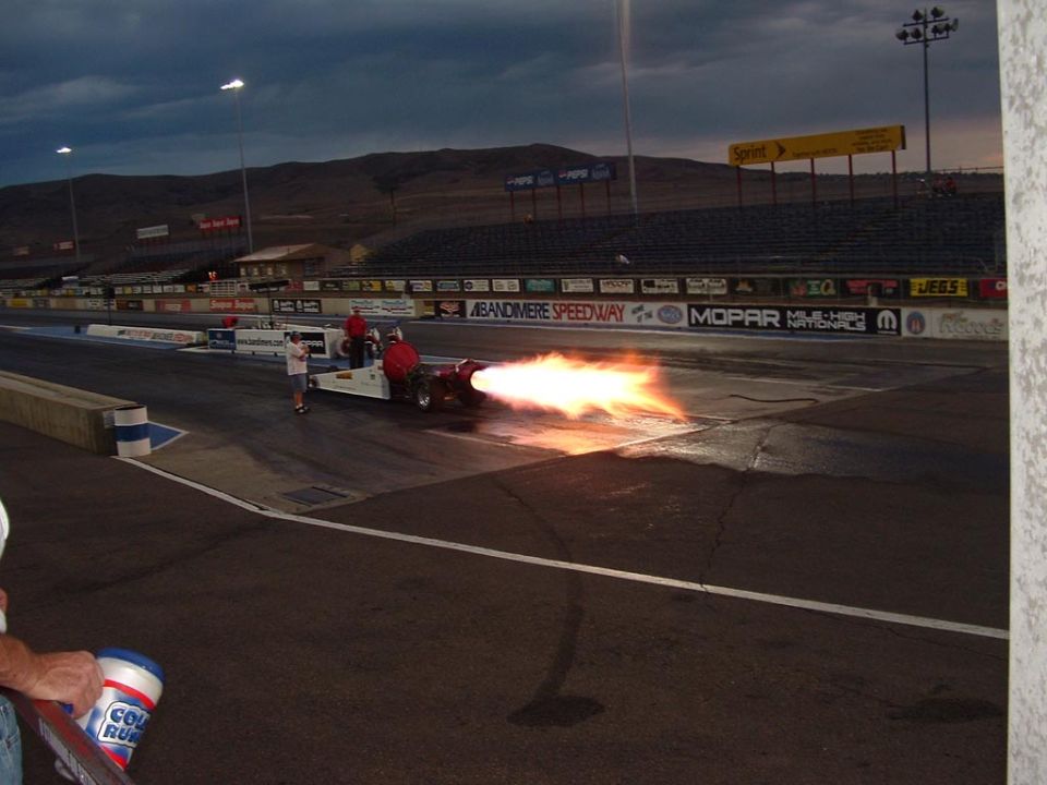 Jet dragster with flames shooting out the back on a race track at dusk