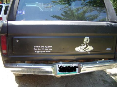 1979 Ford Bronco - Straight-on rear view of a dark Ford Bronco's tailgate and rear glass, showing a white fishing joke decal reading 'It's not how Big your Po…