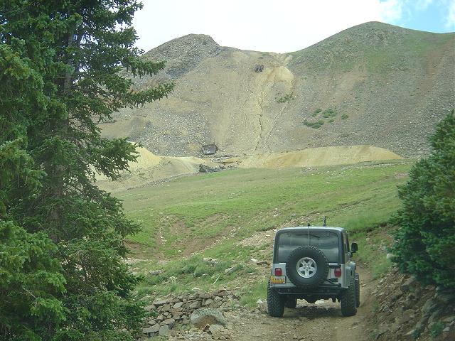 Silver Jeep Wrangler with spare tire on rear door, parked on dirt road