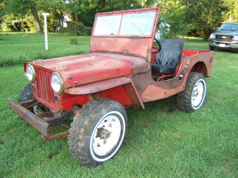 1946 Jeep CJ5 - A vintage red Willys Jeep sits on a grassy lawn, with a modern pickup truck visible in the background.