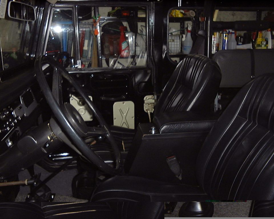 Black interior of 1974 Toyota Land Cruiser with steering wheel, vinyl seats and center console, garage shelves behind