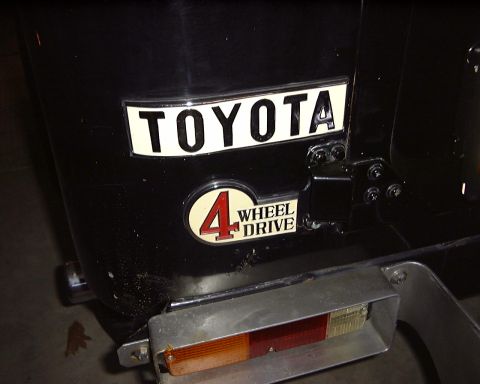 1974 Toyota Land Cruiser - Rear view of a black vehicle showing the Toyota and 4 Wheel Drive emblems, along with a taillight assembly.