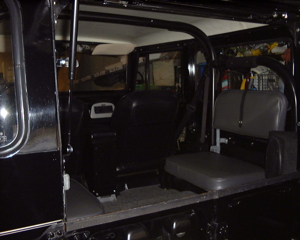 Interior view of a black 1974 Toyota Land Cruiser FJ40 showing front and rear seats, roll cage, and door panel