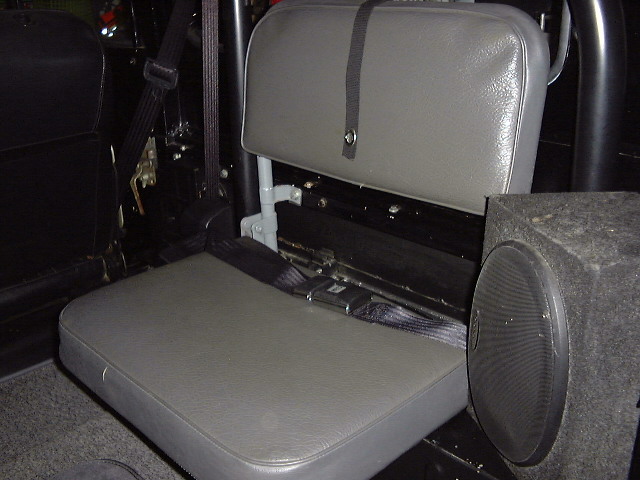 Vehicle interior with grey jump seats, black seatbelts, and a black speaker box. Text 'SUPERMOTORS' is visible