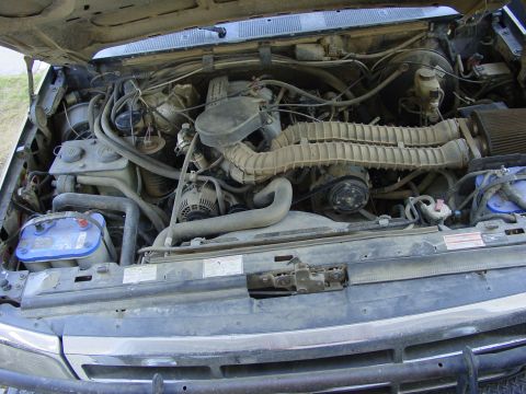1994 Ford Bronco - Overhead engine-bay view of a dusty Ford V8 truck with the hood up, showing the corrugated intake tube running from the air cleaner to the…