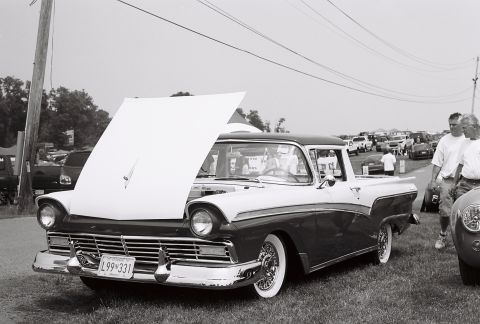 1973 Ford Ranchero - 1957 Ford Fairlane Ranchero at a car show, hood up. Other vehicles and attendees visible.