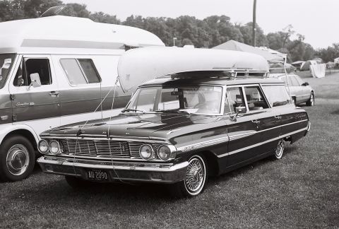 1973 Ford Ranchero - A dark station wagon with a canoe on its roof is parked next to a van and other vehicles.
