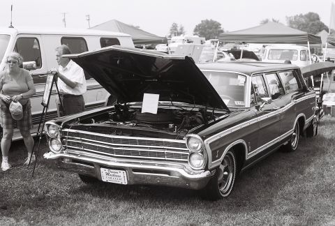 1973 Ford Ranchero - A black station wagon with its hood open is displayed at an outdoor event, with a van and tents in the background.