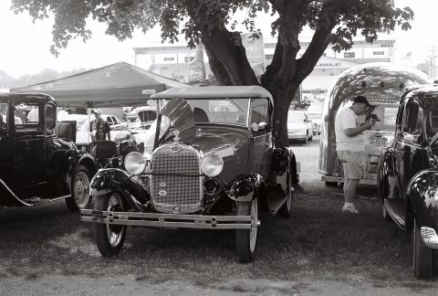 1973 Ford Ranchero - A classic Ford Model A Roadster is displayed at an outdoor event with other vintage vehicles and a trailer.