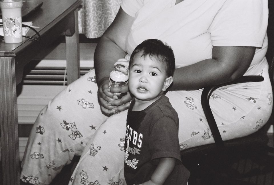 Child in a dark t-shirt sits near a person in patterned pajamas, holding a bottle