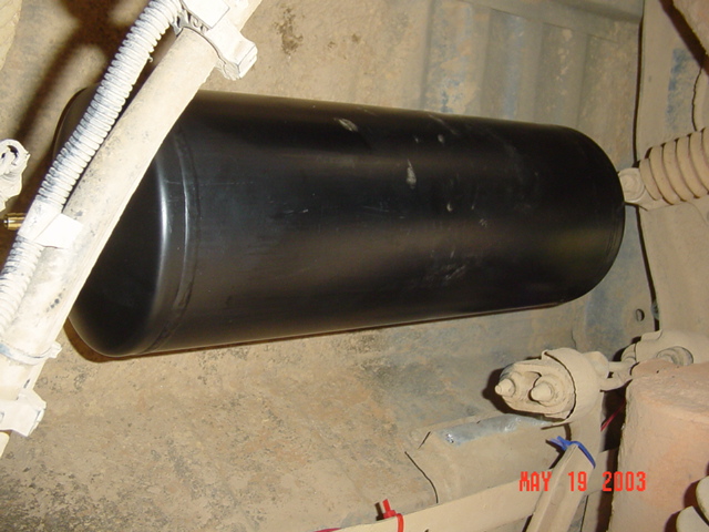 Black cylindrical tank mounted under a vehicle near loomed lines and a leaf-spring shackle