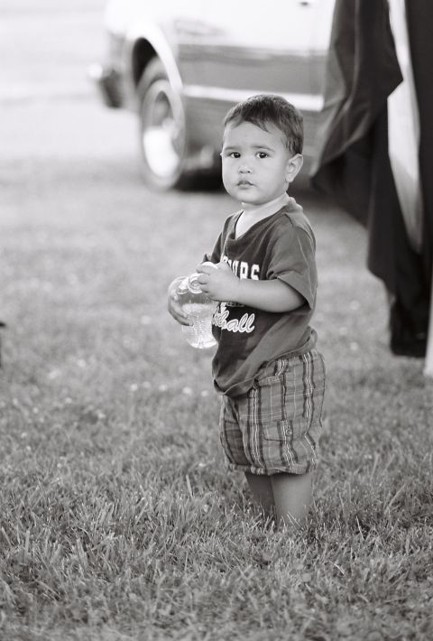 1973 Ford Ranchero - A young child stands in the grass, holding a bottle, with a vehicle partially visible behind them.