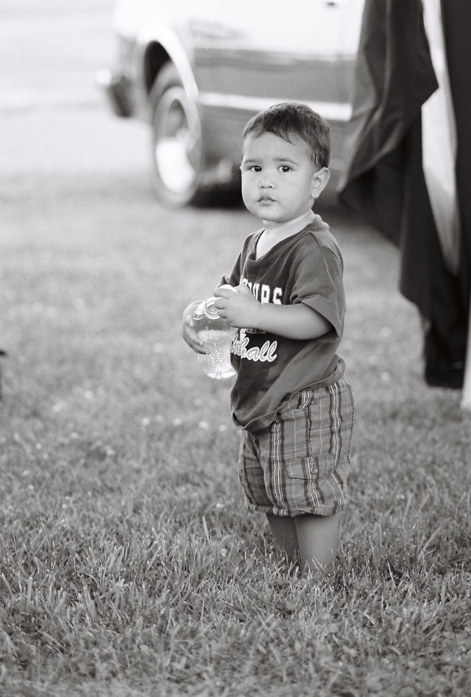 Child holding a bottle, with a car in the background