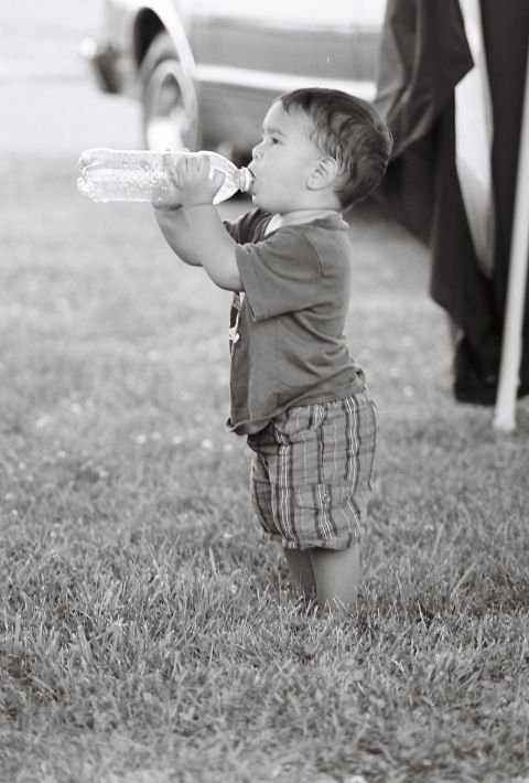 1973 Ford Ranchero - Young child hydrates with a bottle of water on a grassy field, with a vehicle partially visible.